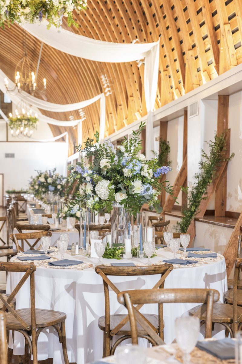 Spring wedding at WinMock at Kinderton, designed by Charming Carolina — reception table with white linen, tall floral arrangement filled with greenery and blooms, and dusty blue taper candles.