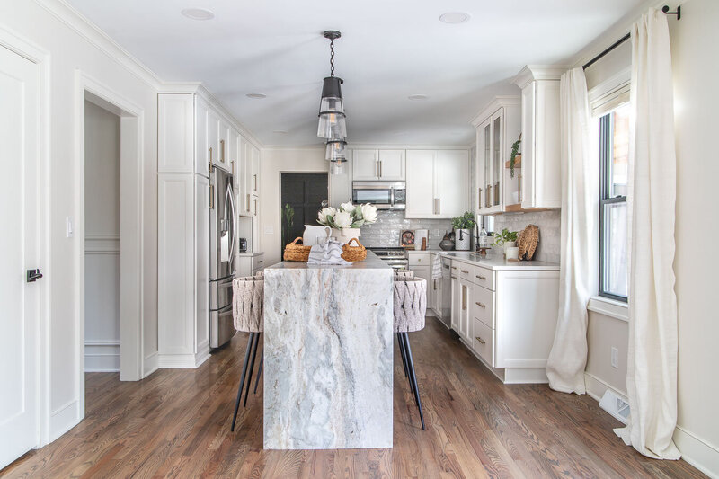 Neutral transitional kitchen with wood flooring and a white marble waterfall kitchen island designed by Chapin interior designer Haven + Harbor