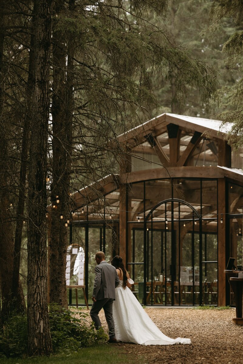 Bride and Groom walking through enchanted forest with stunning Alberta wedding venue in the background.