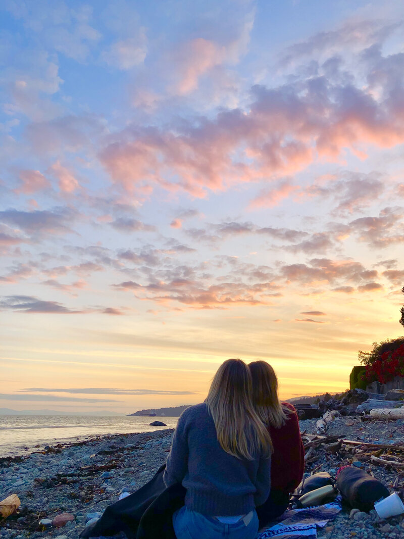 Two friends staring at the sunset while sitting on the beach daydreaming