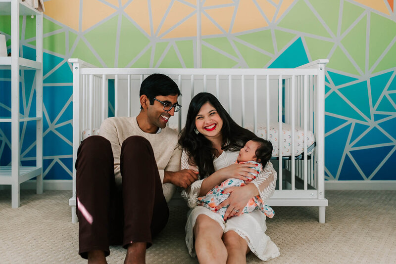 parents laughing and holding their newborn daughter in her nursery