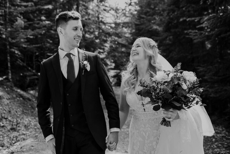 A bride and groom wearing a yellow and green puffy jacket hold each other on top of Rainbow Glacier in Whistler. There is snow all around and blue skies.