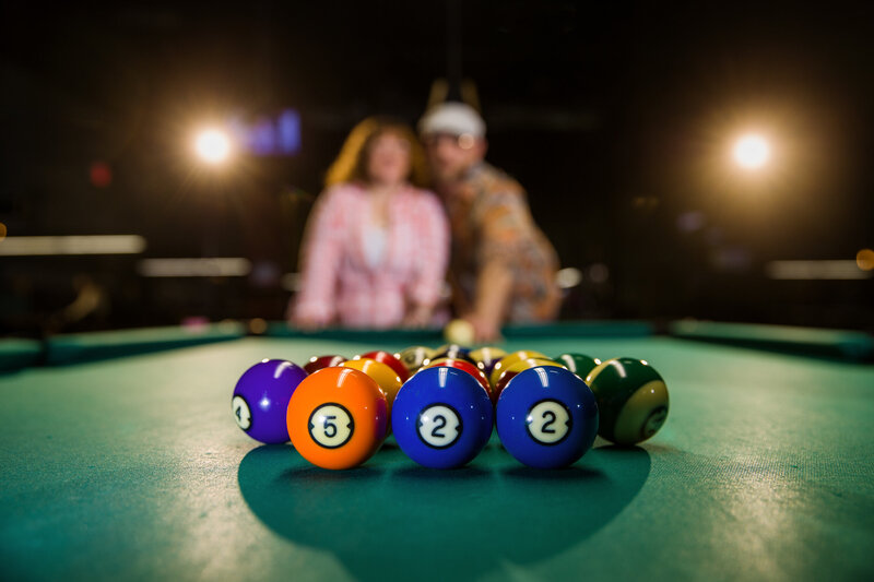 Couple showcasing their chemistry with pool balls and a classic table in this uniquely tailored engagement session.