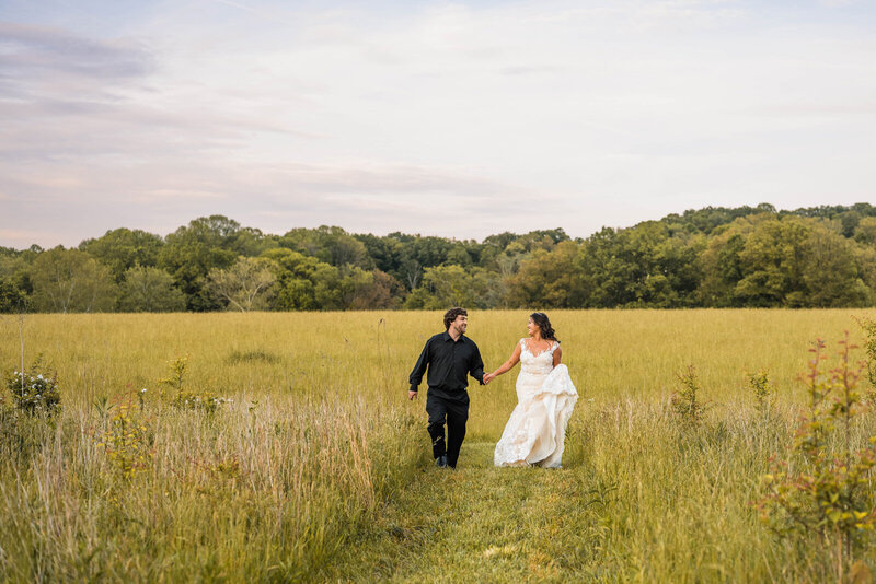 Couple runs happily in a meadow at sunset