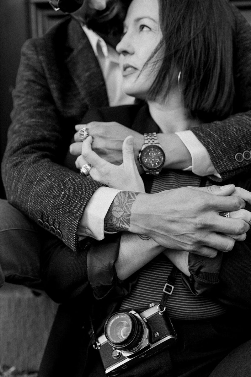 A close up photo of a man hugging a woman from behind, showcasing their rings and watch.