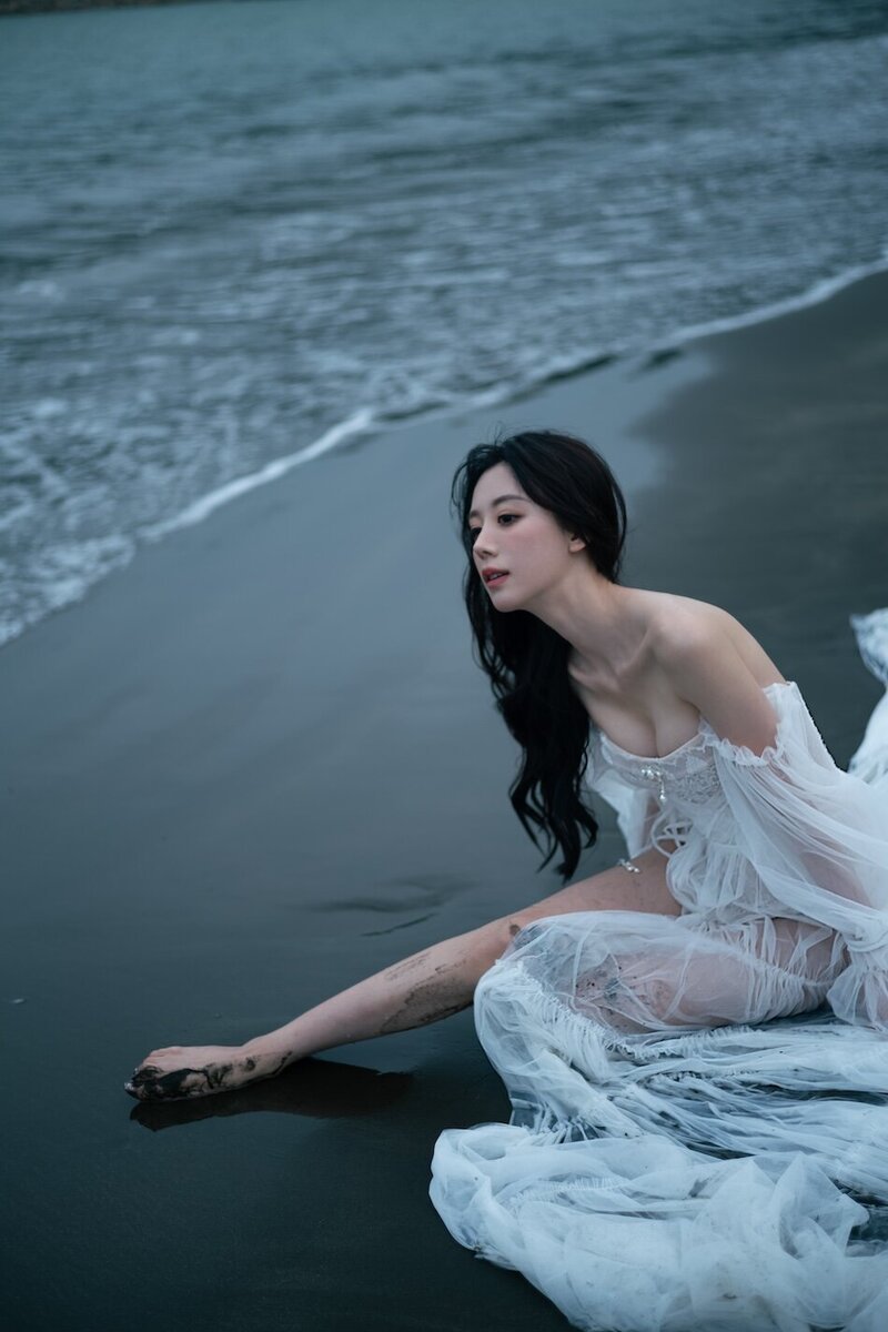 A woman wearing a delicate sheer couture dress shot on the beach in dark moody tones.