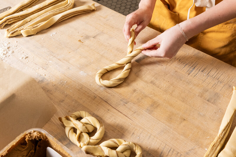 Close-up of baker’s hands braiding gluten-free dough on a wooden work surface at Grain Artisan Bakery in Snohomish, Washington.
