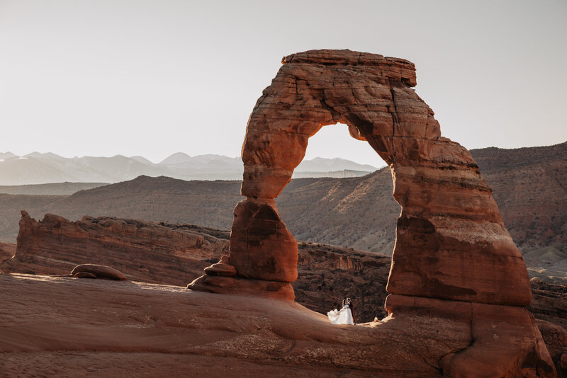Wedding couple standing under Delicate Arch in Moab, Utah for their Arches National Park elopement