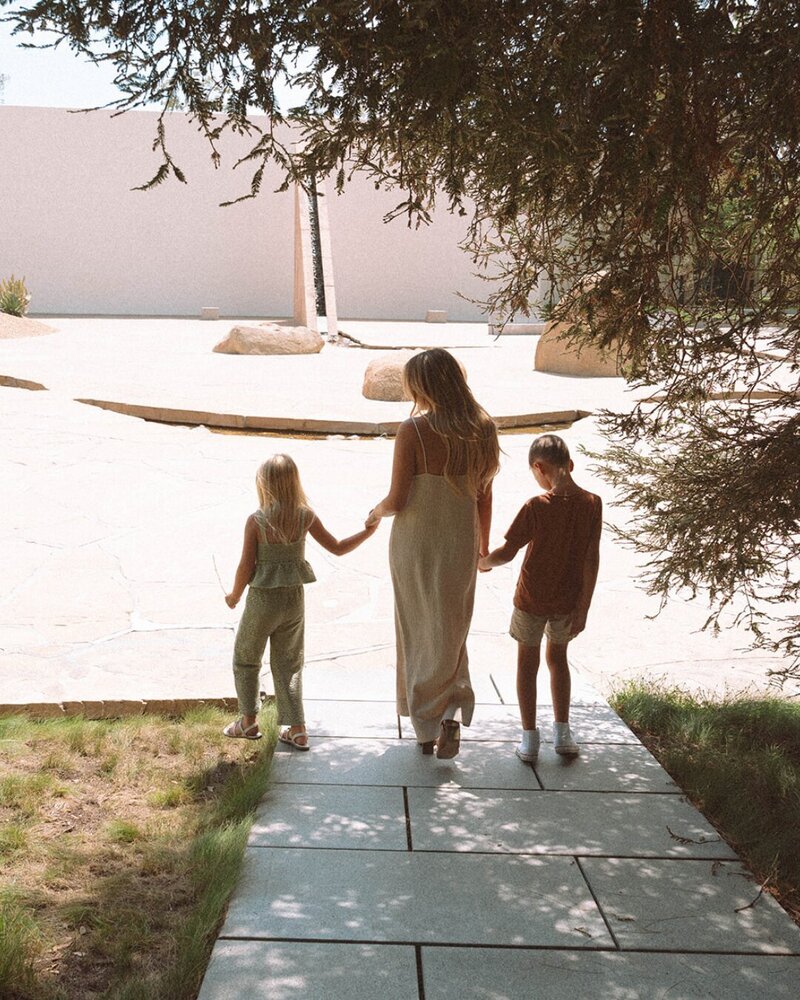 Mom walking hand in hand with her two children at a Costa Mesa garden, photographed in warm natural light.