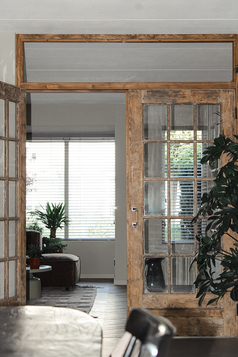 Rustieke houten ensuite deuren die karakter en warmte toevoegen aan een moderne woonkamer, met veel lichtinval en natuurlijke elementen.