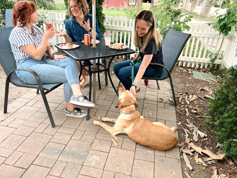 Three women out to lunch at an outdoor restuarant while dog is in a down