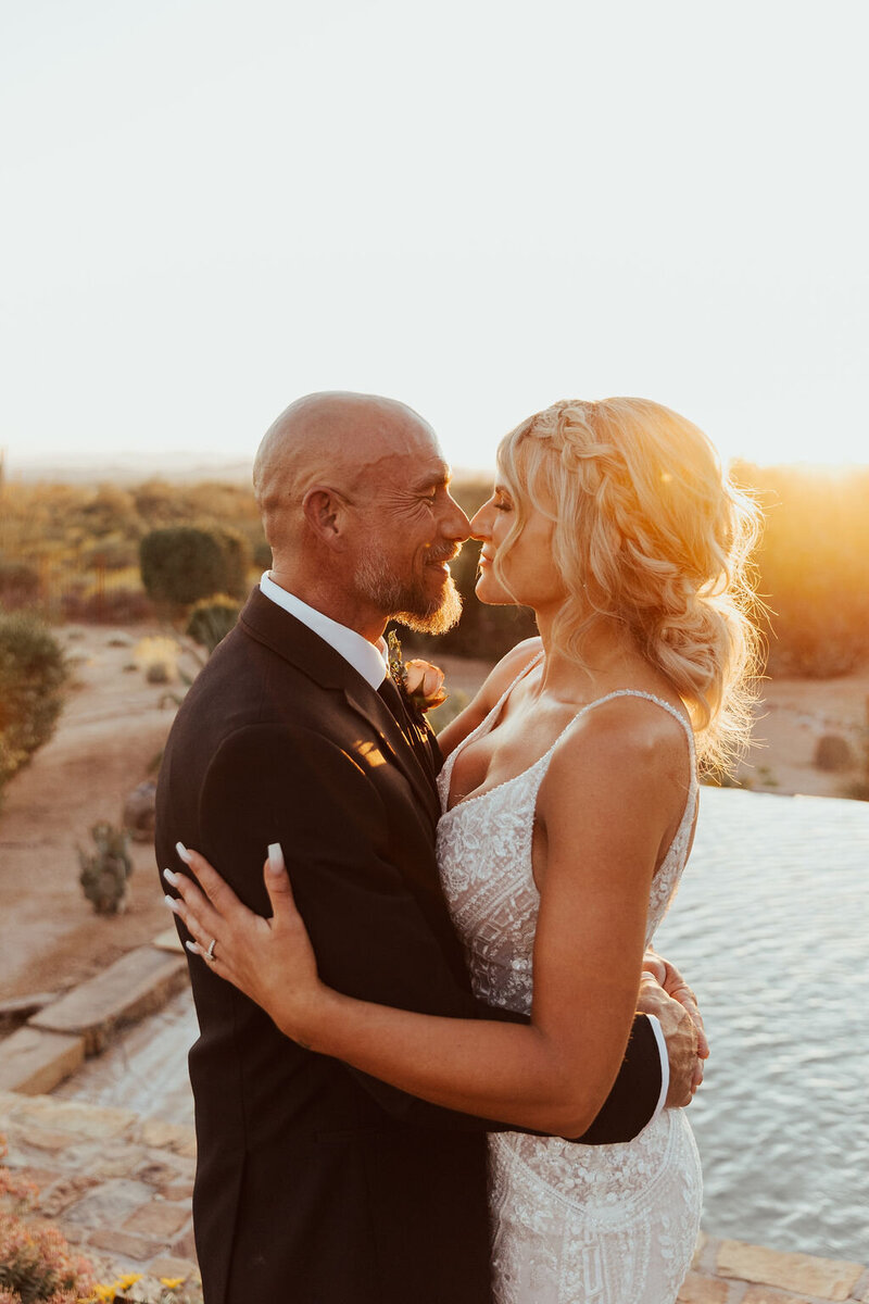Newlywed couple embraced by the pool with the sunset in the background
