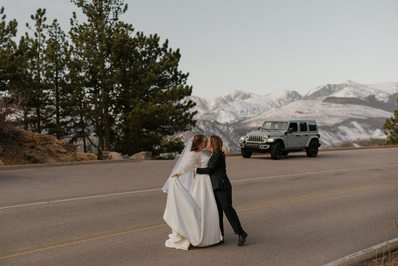 A newlywed couple kissing on a mountain road 