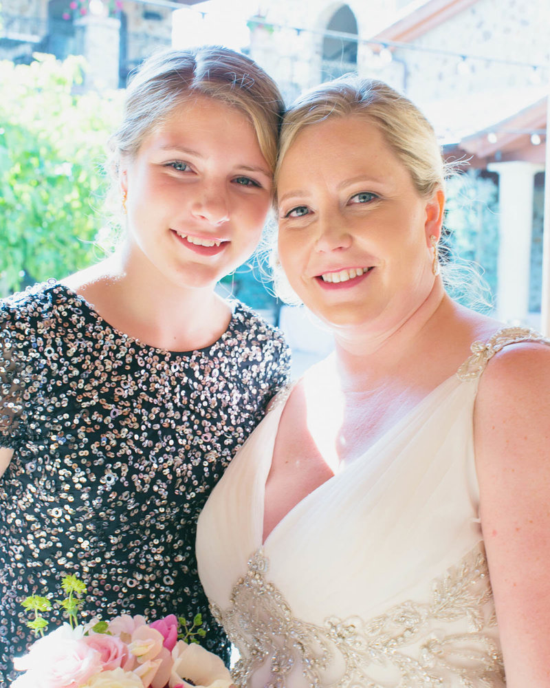 Bride stands with Bridesmaid touching heads smiling at the camera
