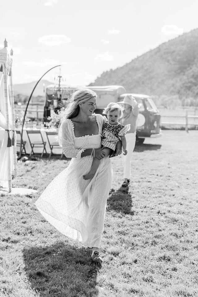 woman in flowing white dress carrying child on her hip