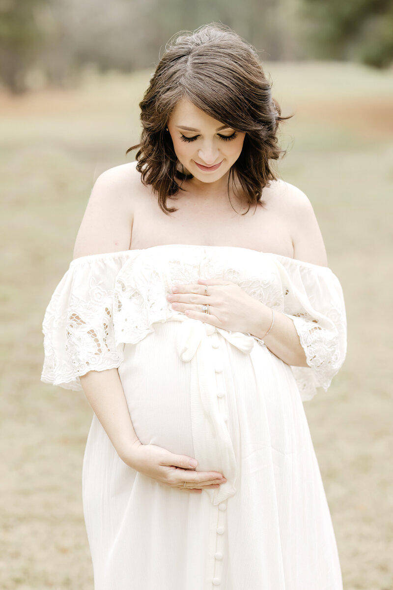 Pregnant woman looking down at belly in white dress