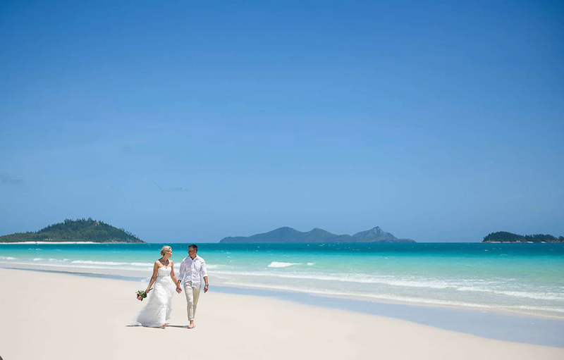 A bride and groom walking along the beach after eloping