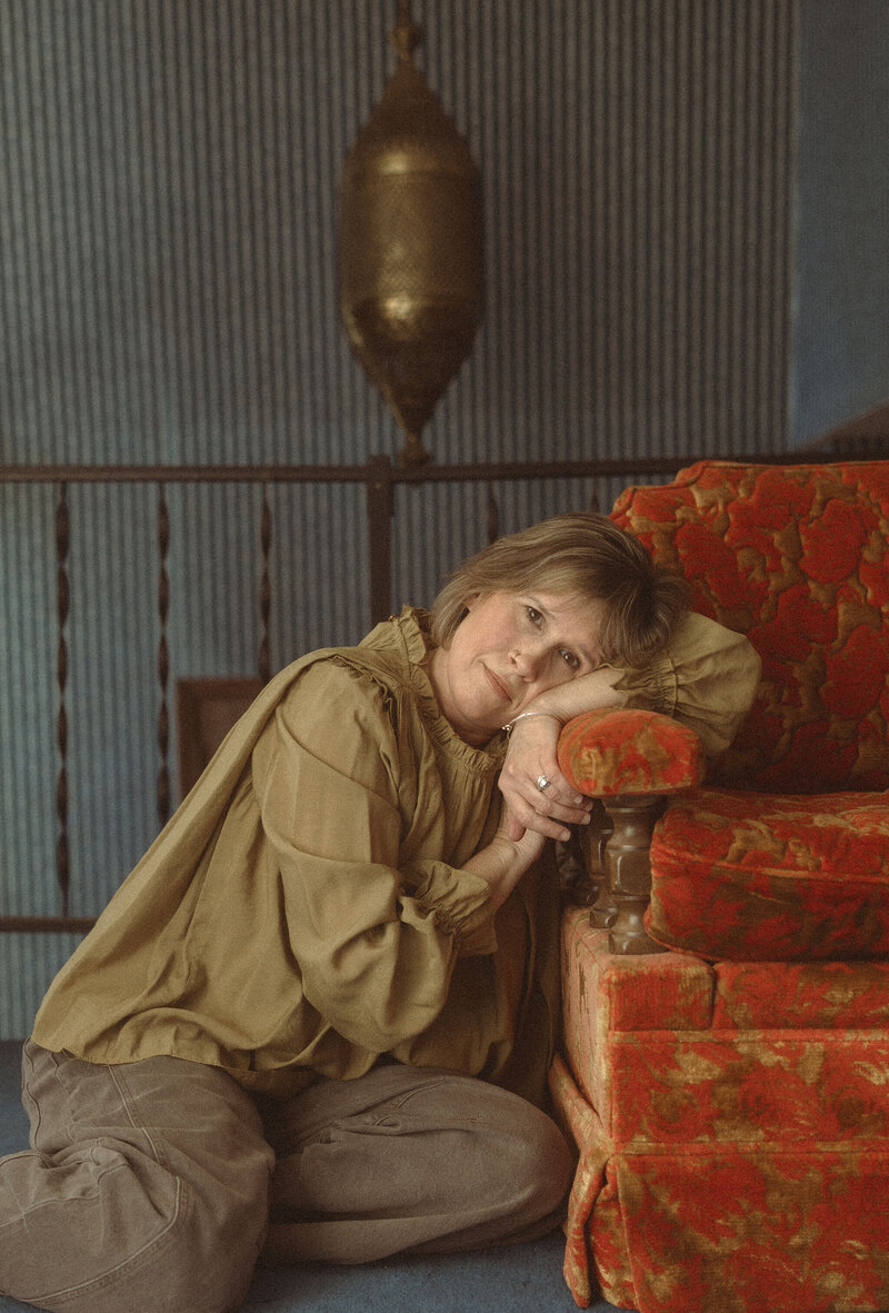 Photographer Melanie Dalton leaning on a red antique sofa. 