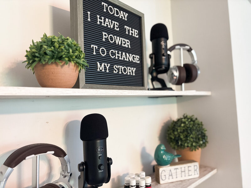 Motivational quote sign with headphones, podcast mic, and greenery on styled workspace shelf