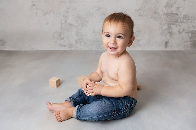 Smiling one year old baby boy playing with wood blocks for his studio birthday session with Jamie Englert Photography.