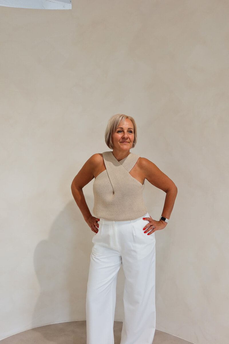Sharron, sober coach and founder of Midlife Sober Glow, standing confidently in a beige top and white trousers against a neutral background.