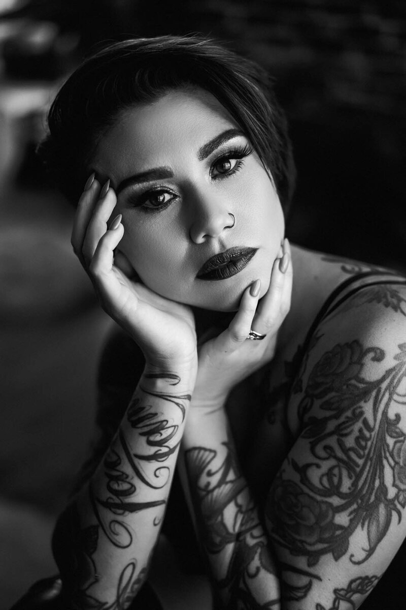 A woman looks into the camera and shows off her arm tattoos for a boudoir photography in vancouver photoshoot