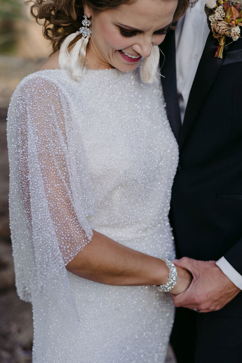 Bride with beaded white wedding dress and sleeves, holding the hand of her groom