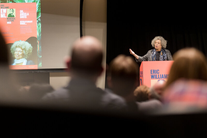 A woman points at a presentation on a screen while standing in front of a podium