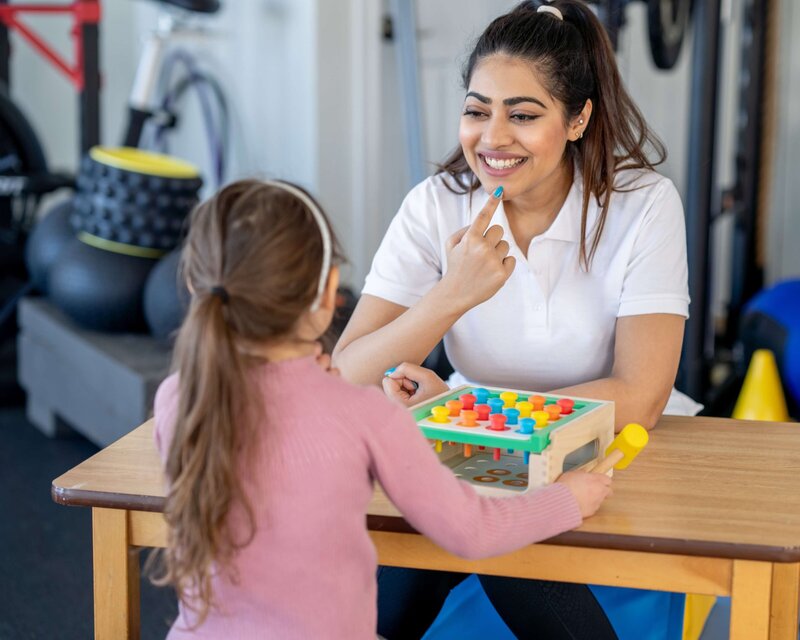 A speech language pathologist working with a school aged girl on articulation exercises during her speech therapy session