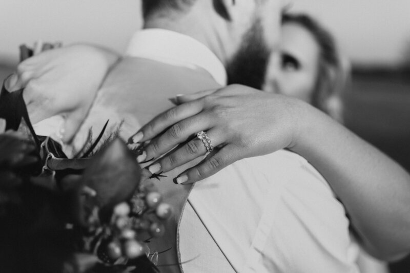 A wife's hand is on her husband's shoulder, showing off her wedding ring.