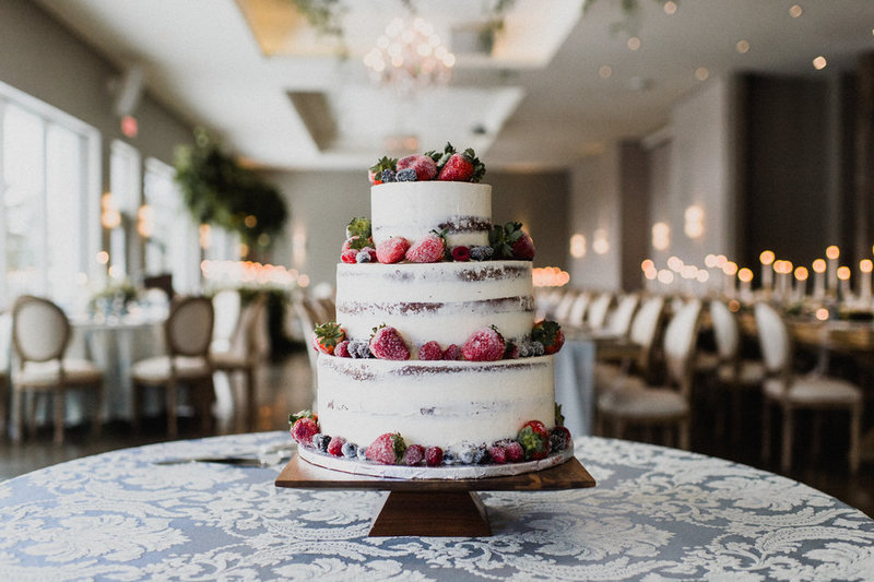 A 3 tiered, frosted berry wedding cake on a wooden pedastal