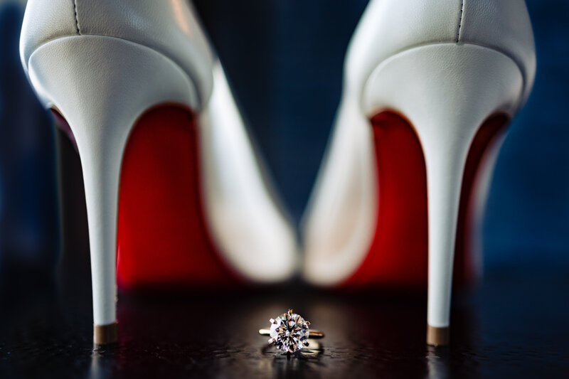 A very large diamond engagement ring sitting between a pair of Lou Botian heels