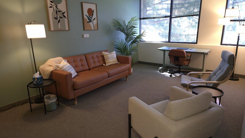 Office including brown leather couch, white chair, and sea foam green wall with grey carpet 