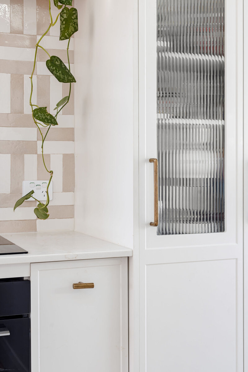 A modern kitchen by a renowned Newcastle interior designer features a textured glass cabinet, climbing plant, and checkered backsplash, epitomizing luxury home design in Newcastle with its elegant and sophisticated touch.
