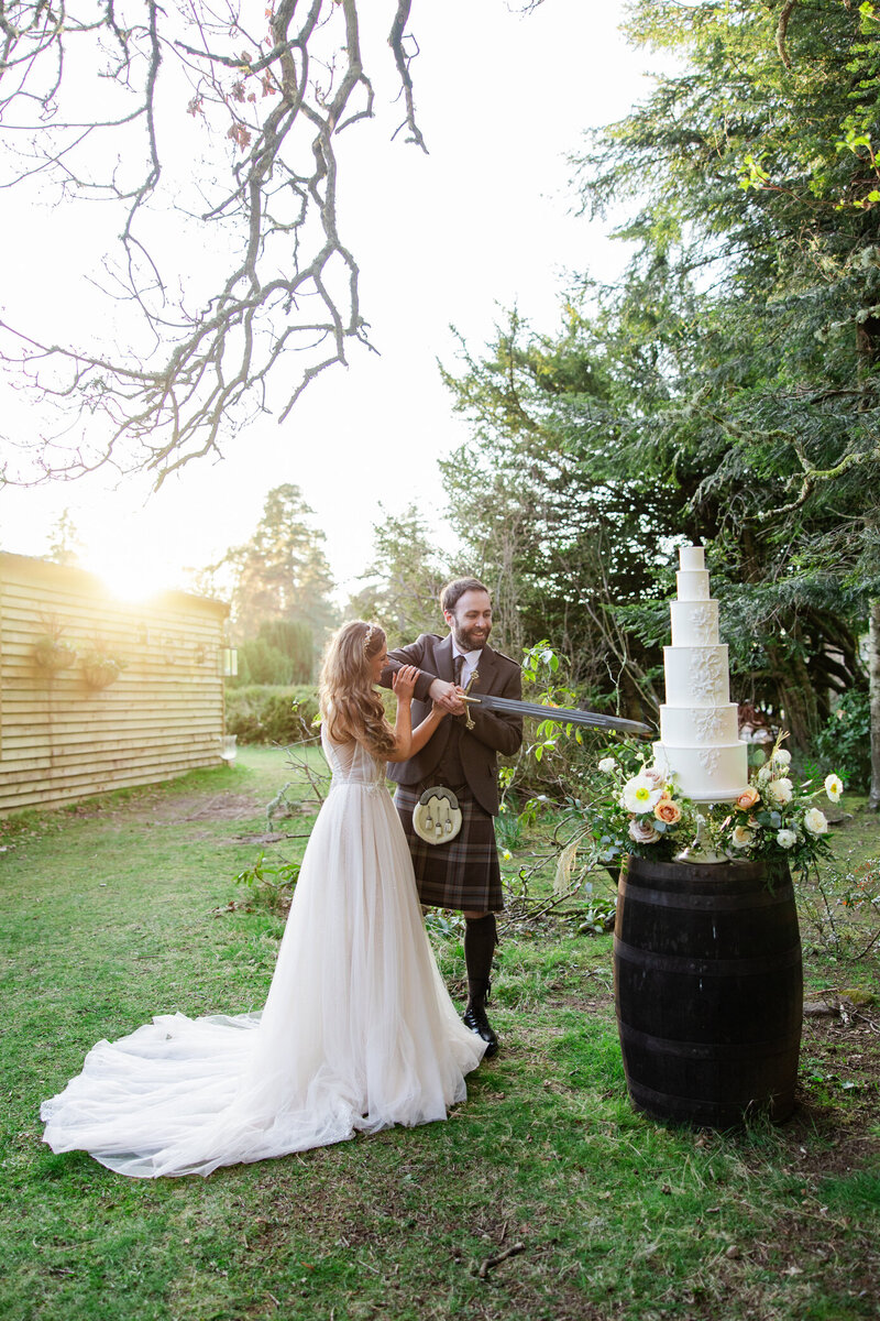 kilt wearing groom and bride cut cake with sword