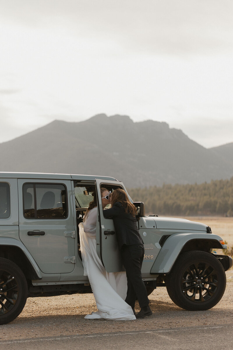 A newlywed couple kissing through a slightly open Jeep door 