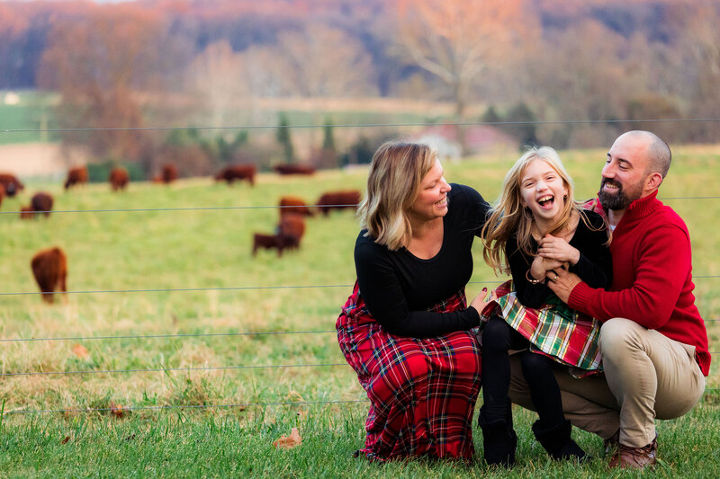 A family of three has a tickle fight and laughs together at a farm.