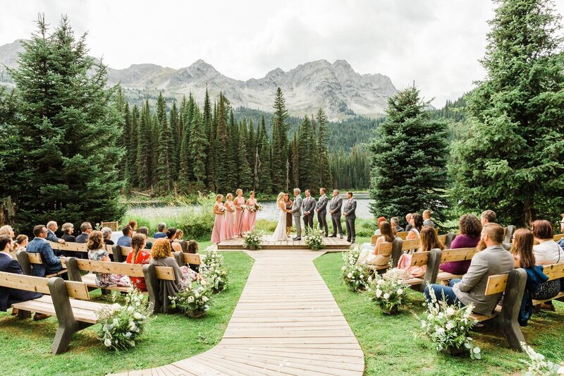A beautiful ceremony photograph of a bride and groom surrounded by bridesmaids and groomsmen at Island Lake Lodge in Fernie, framed by breathtaking mountain views.