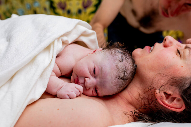 Mother delivering the placenta after water birth at Toronto Birth Centre, supported by her partner, baby resting on her chest.
