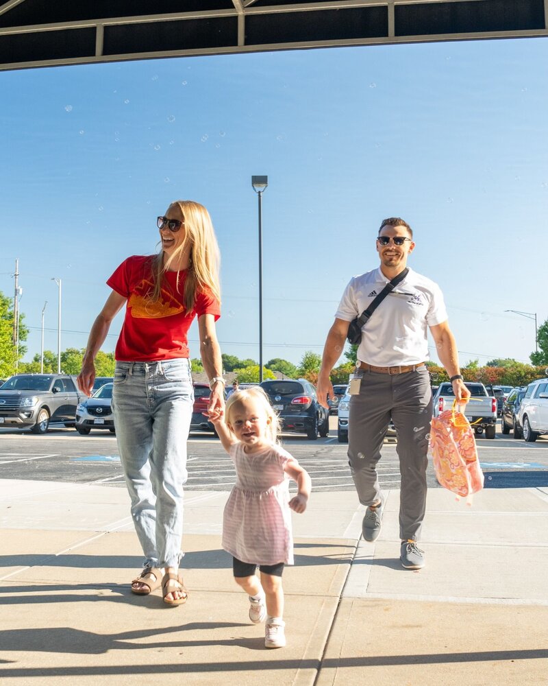Family walking into church from parking lot, mother is holding toddlers hand and father follow behind.