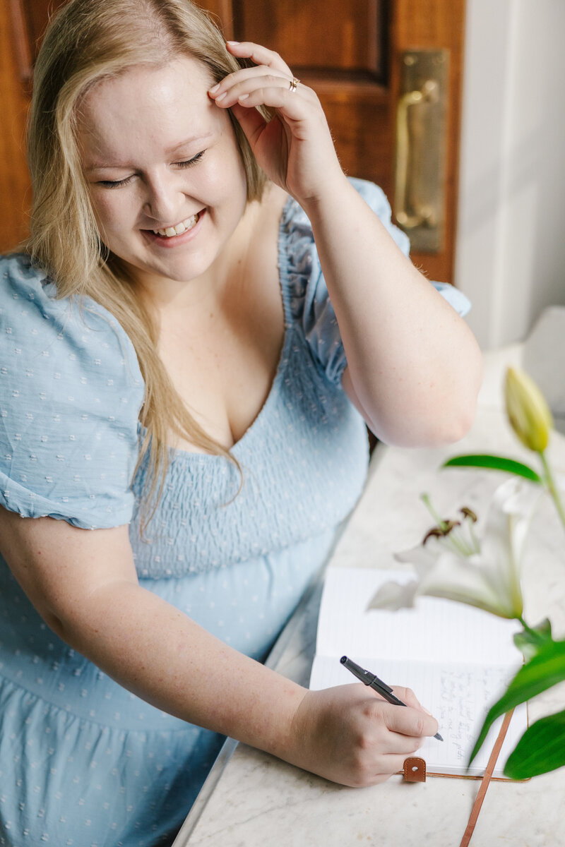 Woman in a light blue dress writing in a notebook at a desk
