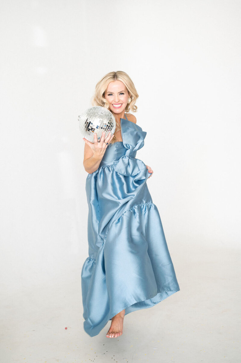 Woman in blue satin dress with big bow holds disco ball