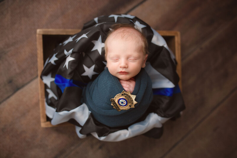baby boy sleeping in a basket with a black and blue police flag
