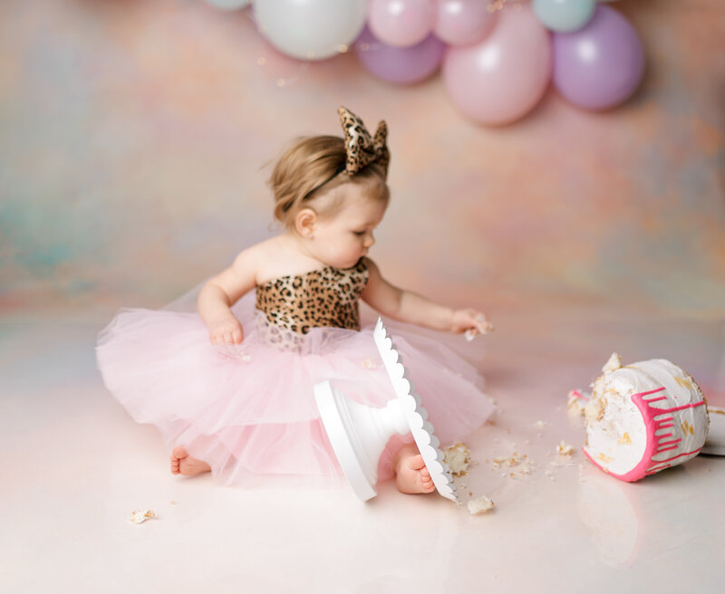 One year old girl in tutu looking at fallen cake