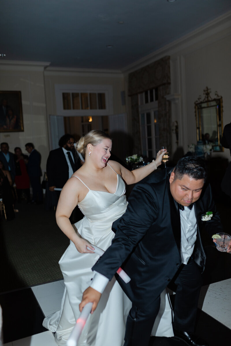 A joyous wedding reception dance moment, featuring the bride pulling the groom onto the dance floor.