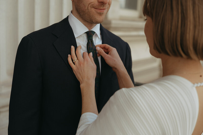 bride fixing groom's tie outside of city hall after eloping shot by Elsie Goodman Photography | NYC Elopement Packages