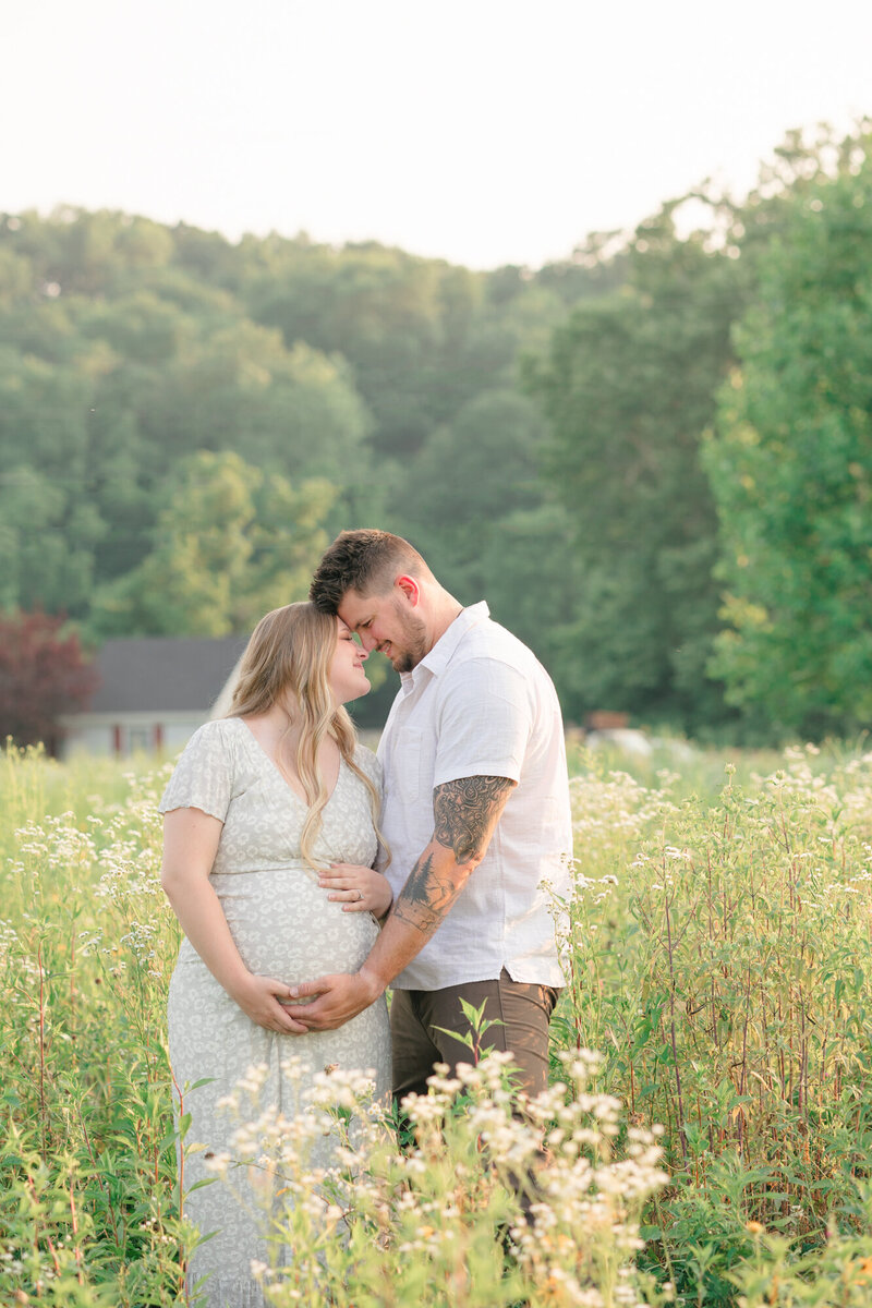 Expecting mom and dad standing in a field of wildflowers taken by newborn photographer Missy Marshall