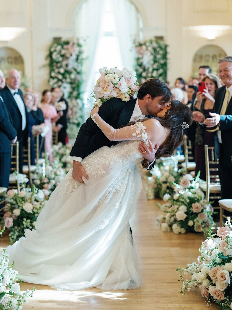 Below the waste close up of bride and groom holding hands and bouquet