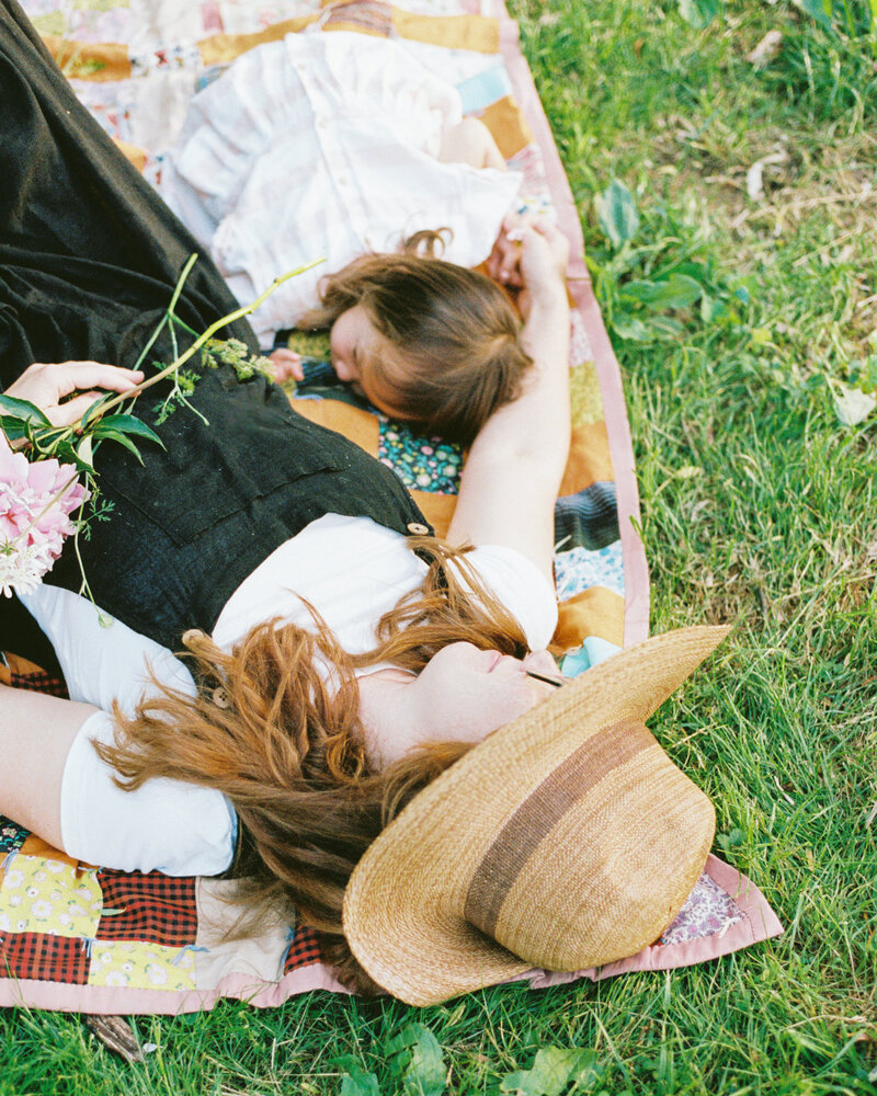 Mom and daughter lay on grass on top of a quilt
