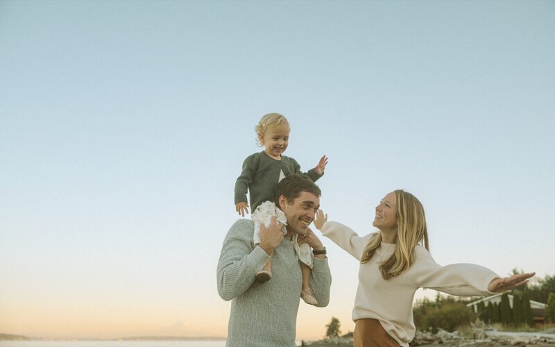 male and female playing with daughter at beach during golden hour